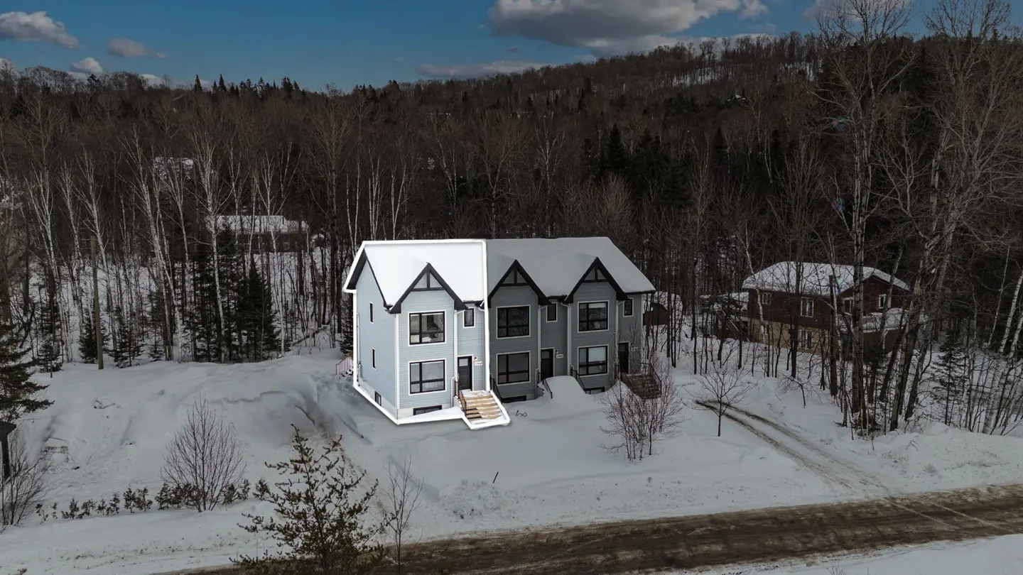Gray townhouse with black trim and snow-covered roof, surrounded by snow and trees.