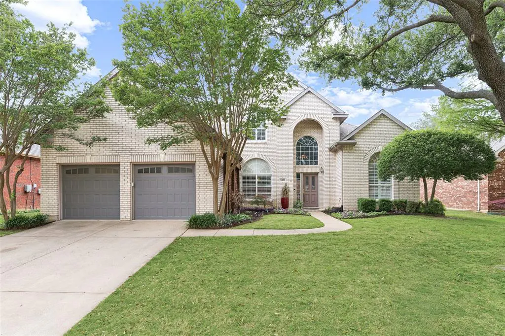 Two-story brick house with gray garage doors, arched windows, and a well-manicured lawn.