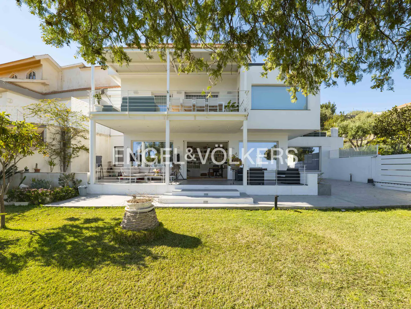Two-story white house with a lawn and an Engel & Völkers sign on the ground floor.