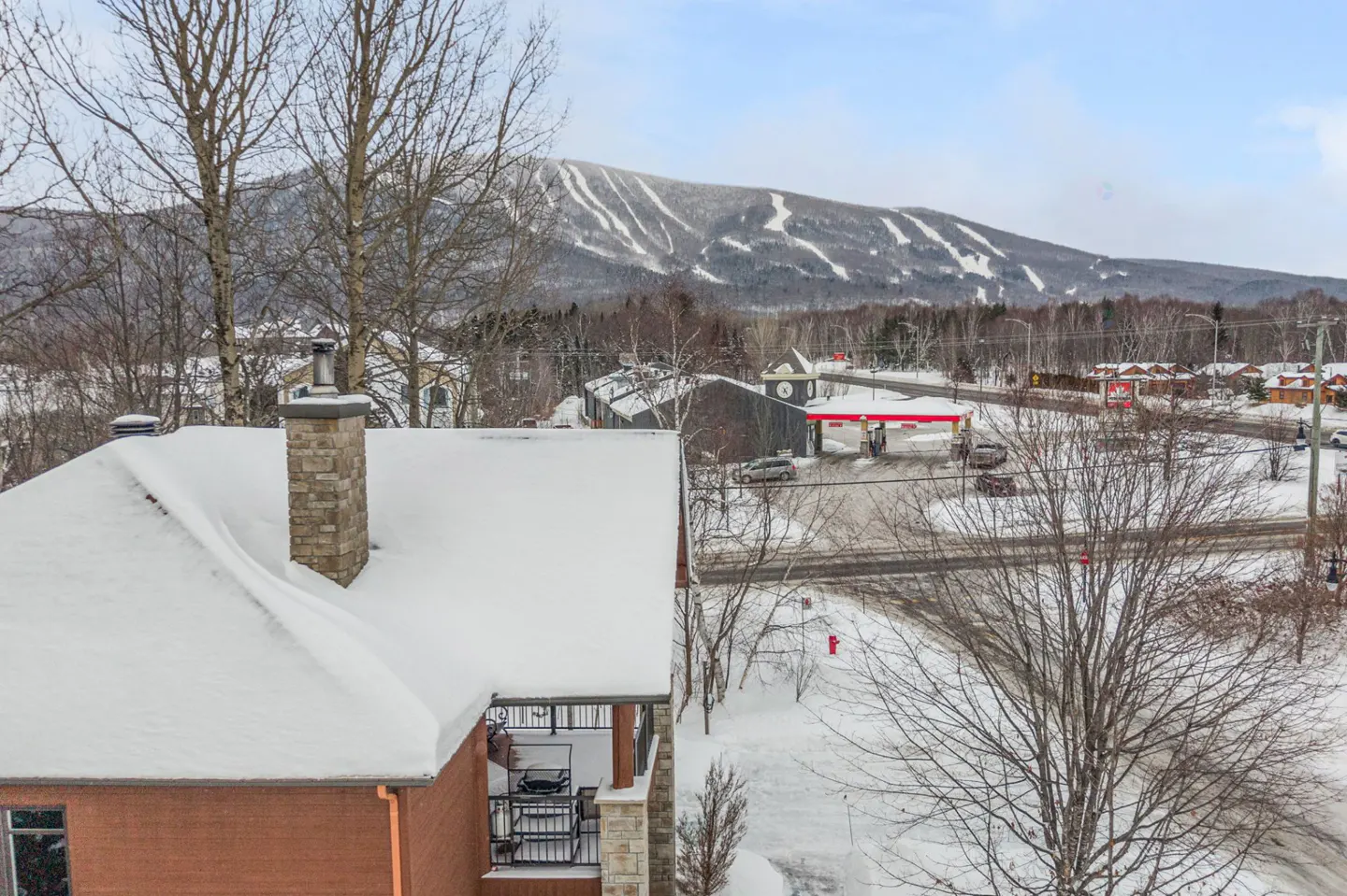 View from a snow-covered roof of a brick house, with a mountain and ski runs in the background.
