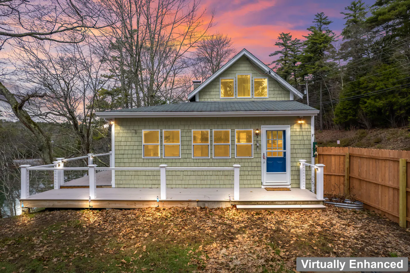 Exterior view of a light green shingle house with a blue door and white trim, set against a colorful sunset sky.