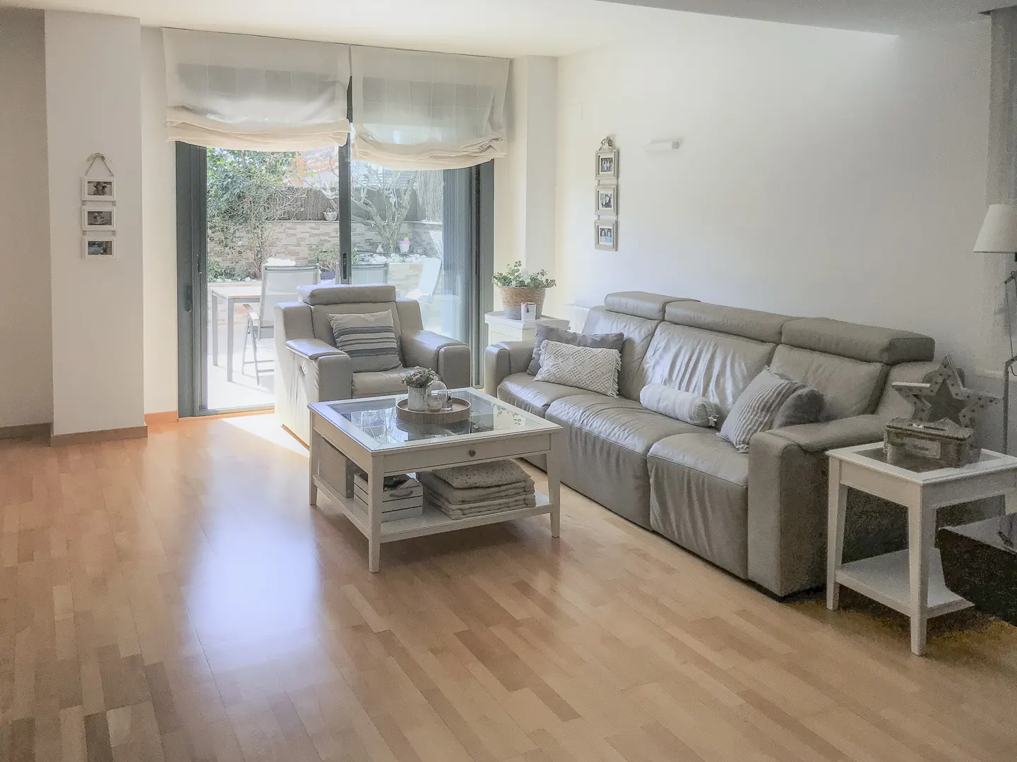 Living room with light wood floors, a gray leather sofa, armchair, and a glass-topped coffee table. Sliding glass doors lead to a patio.