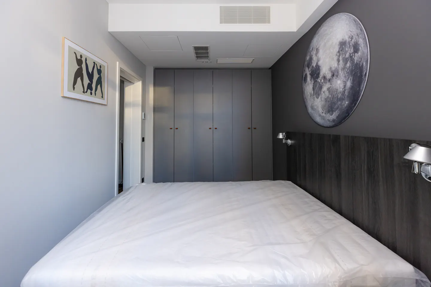 Bedroom with a bed covered in plastic, gray walls, a moon art piece, and a gray wardrobe.