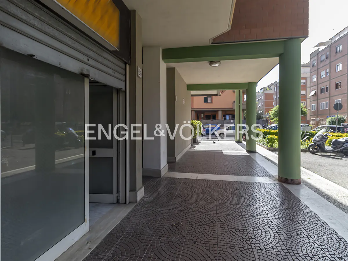 Exterior view of a commercial space with a gray metal roll-up door and a covered walkway with green columns.