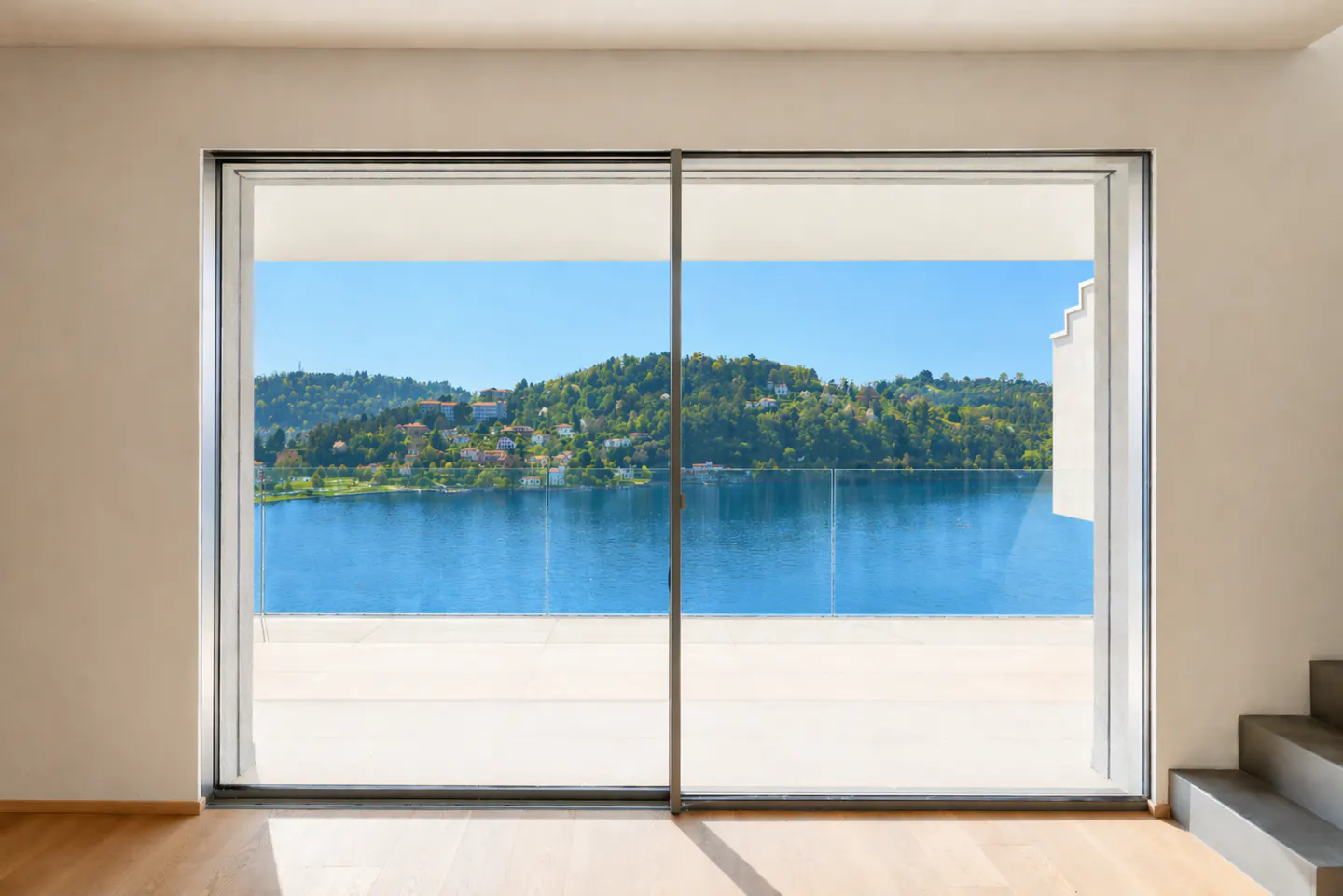A bright room with a large sliding glass door reveals a scenic lake view. Blue water and green hills are visible.