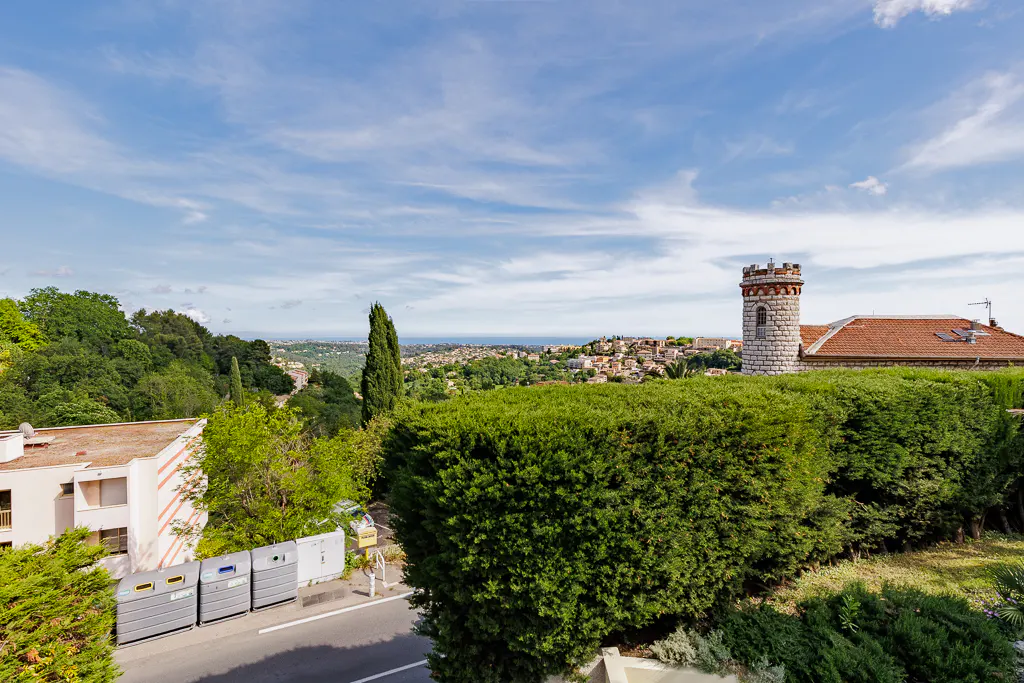 View of a European town with a stone tower, green trees, and a blue sky with clouds.