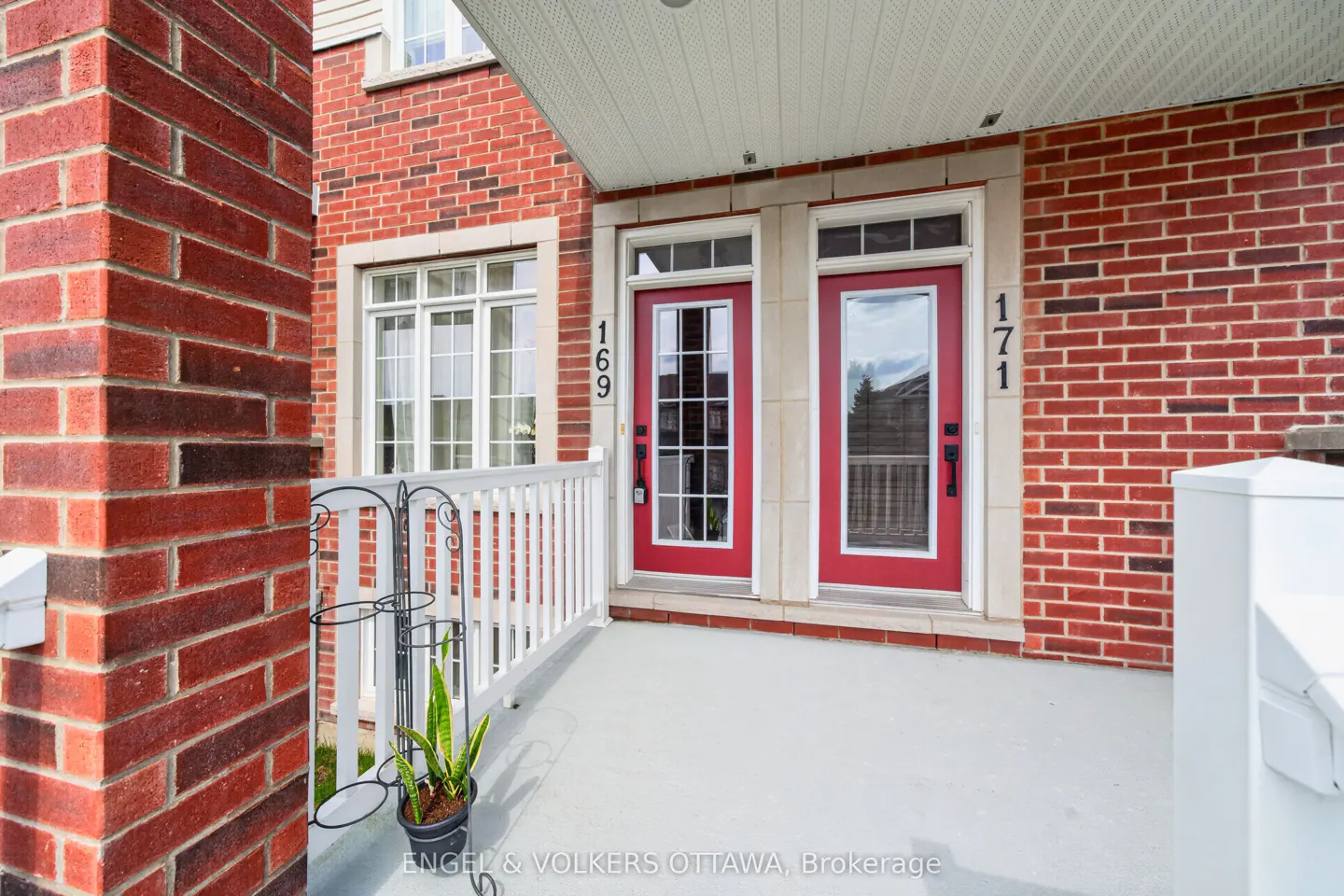 Exterior view of a red brick townhouse with two red doors, numbered 169 and 171, and a white porch with a plant.