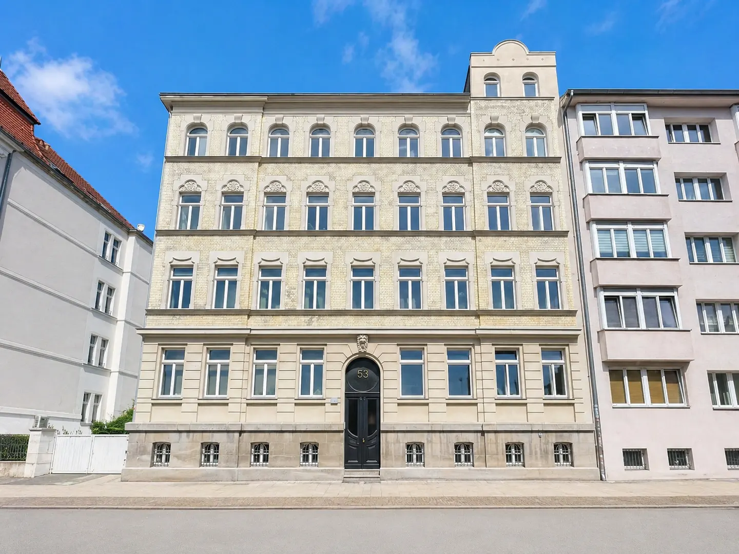 A four-story, light-colored historic apartment building with a central arched black door numbered 53 under a blue sky.