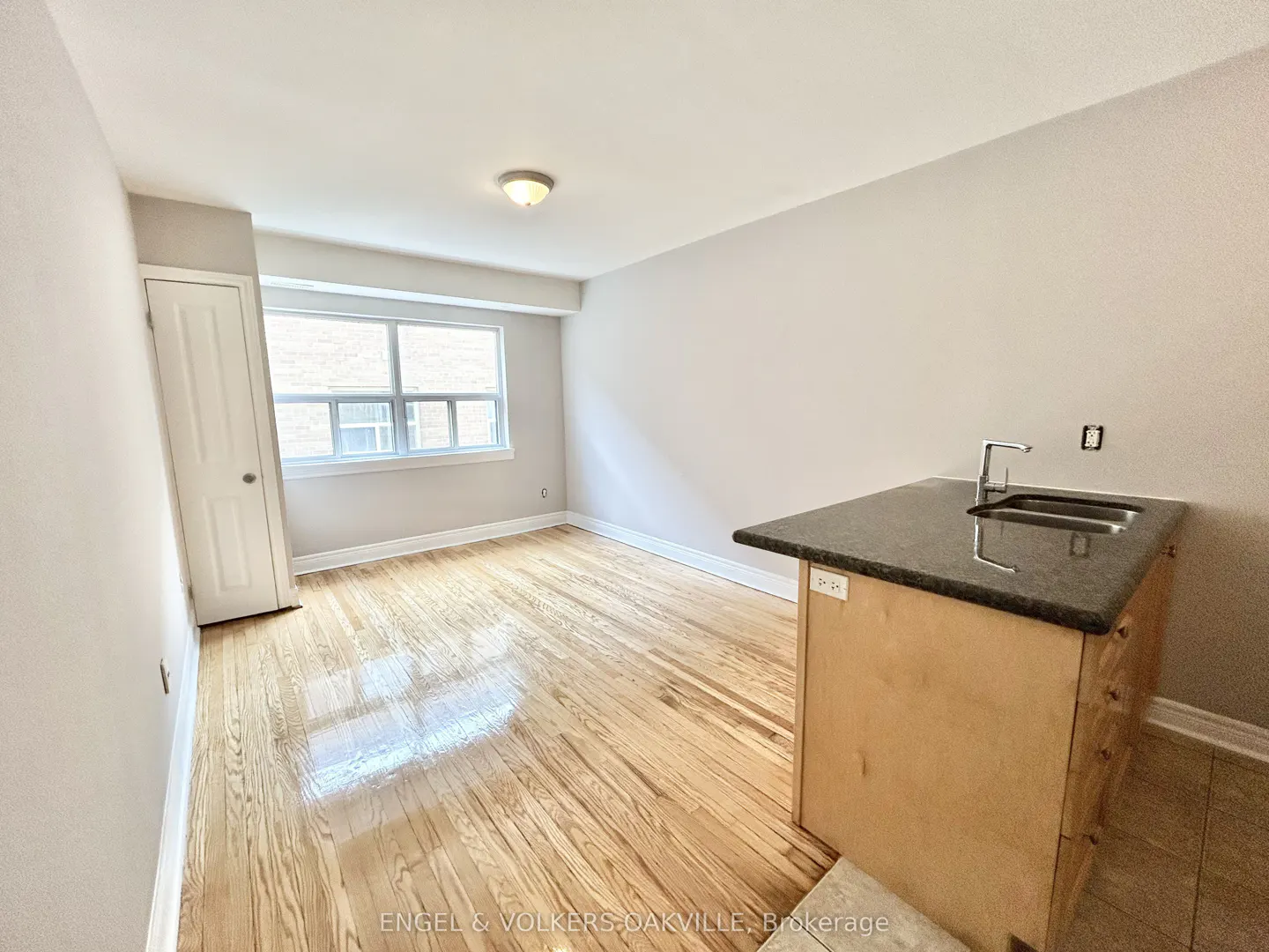 Bright studio apartment with hardwood floors, a window, and a kitchen island with a sink.