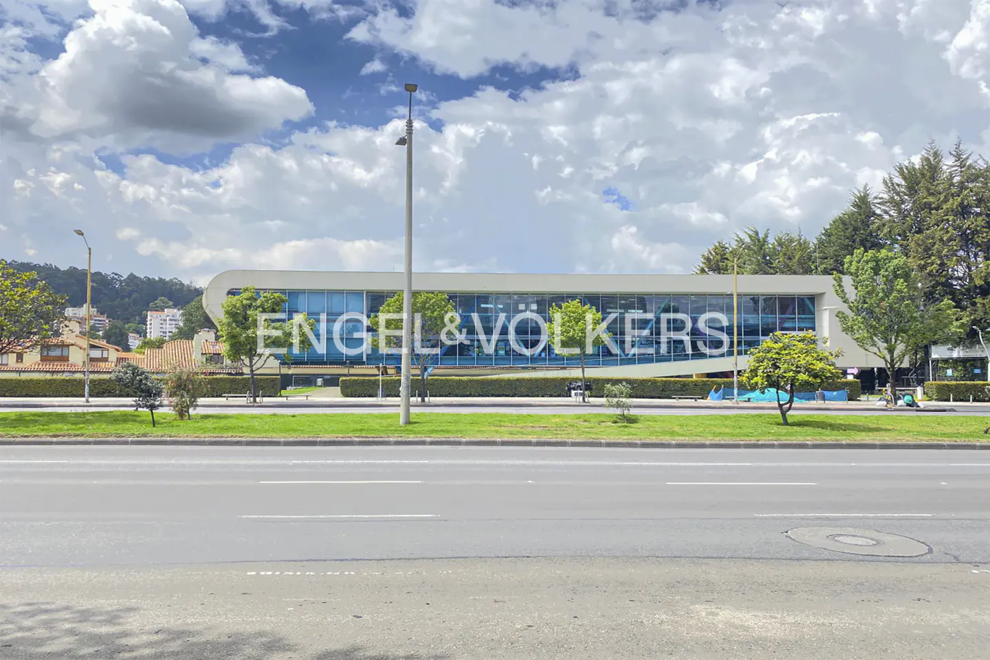 Engel & Völkers office building with blue glass windows and white frame, viewed from across a gray asphalt road.