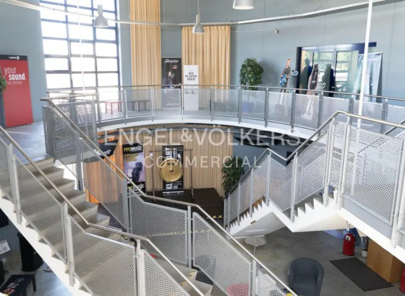 Multi-level commercial space with metal stairs and railings. Stage with gong, posters, and Engel & Volkers logo visible.