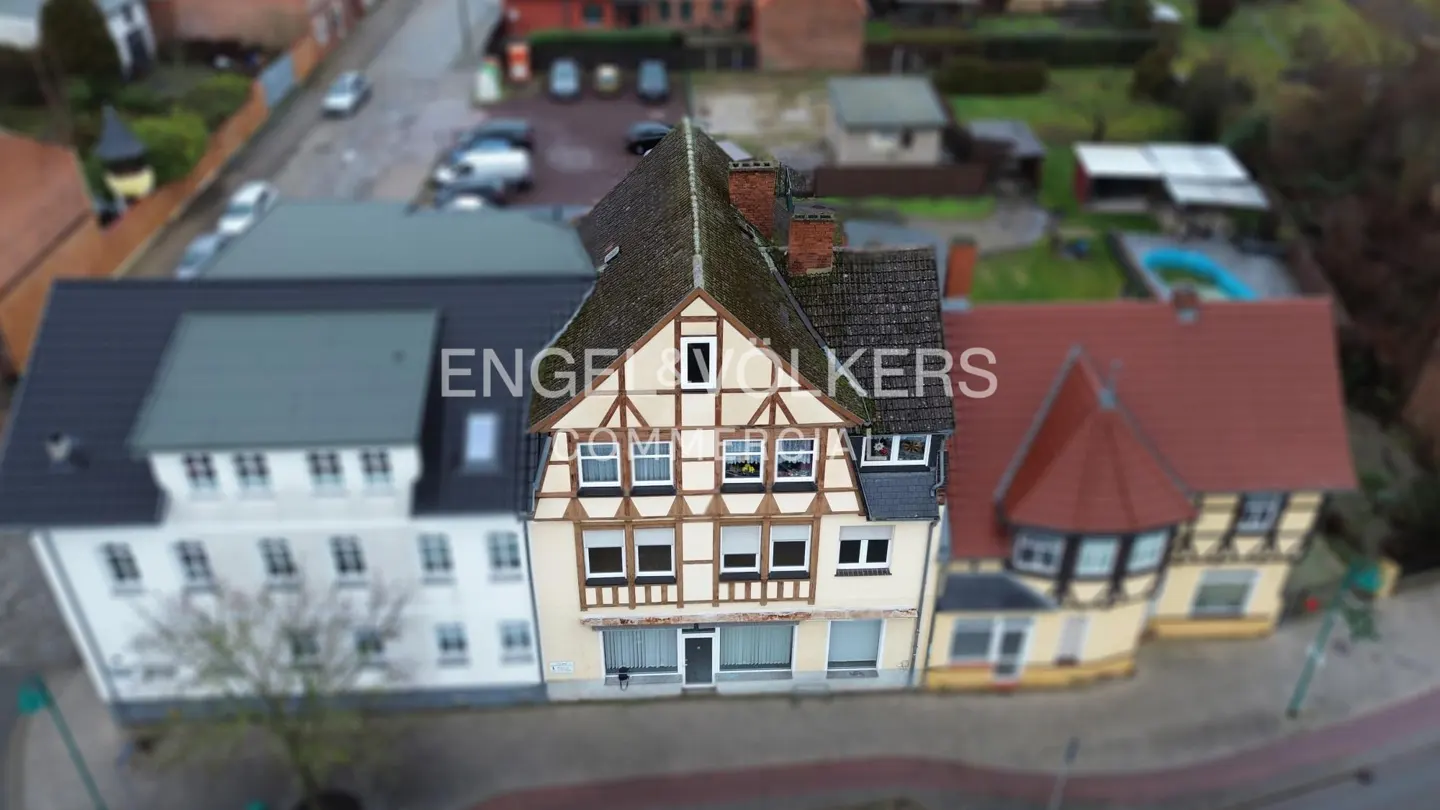 Aerial view of a half-timbered building with a brown roof, flanked by white and red brick buildings. Engel & Volkers logo visible.