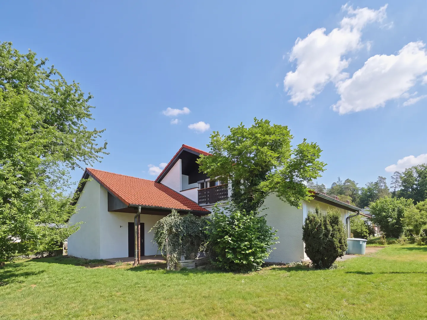 Exterior view of a white house with a red tile roof, green lawn, trees, and a blue sky with white clouds.