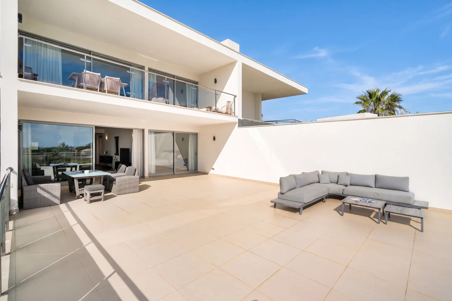 Two-story white house with a large patio. Patio furniture includes a gray sofa and a wicker dining set. Blue sky background.