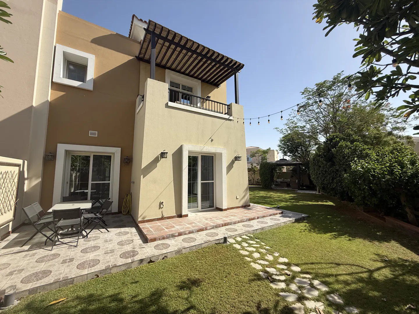 Two-story tan house with a balcony and a patio with a table and chairs in the backyard.
