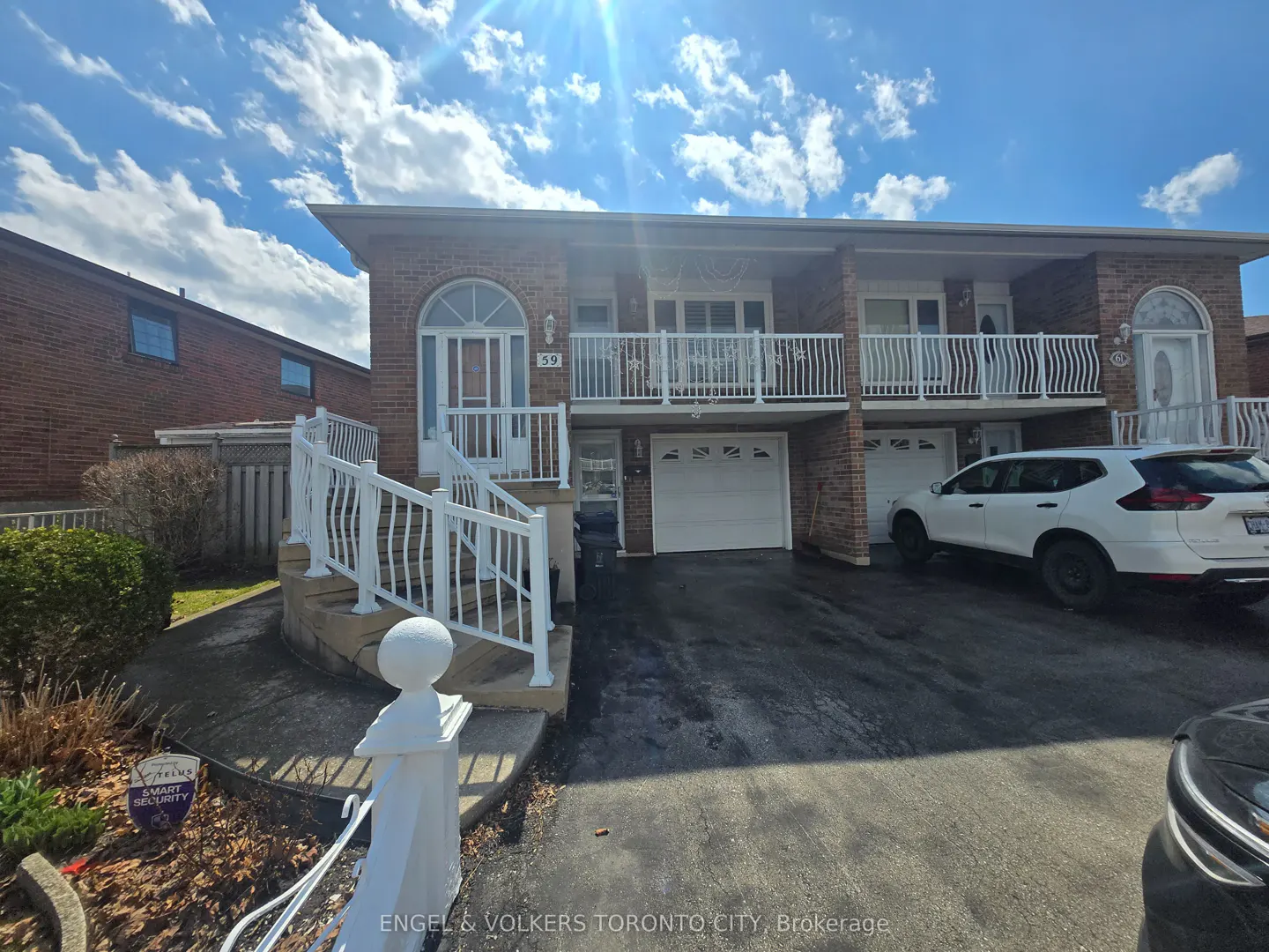 A two-story brick duplex with white railings and a white car parked in the driveway.