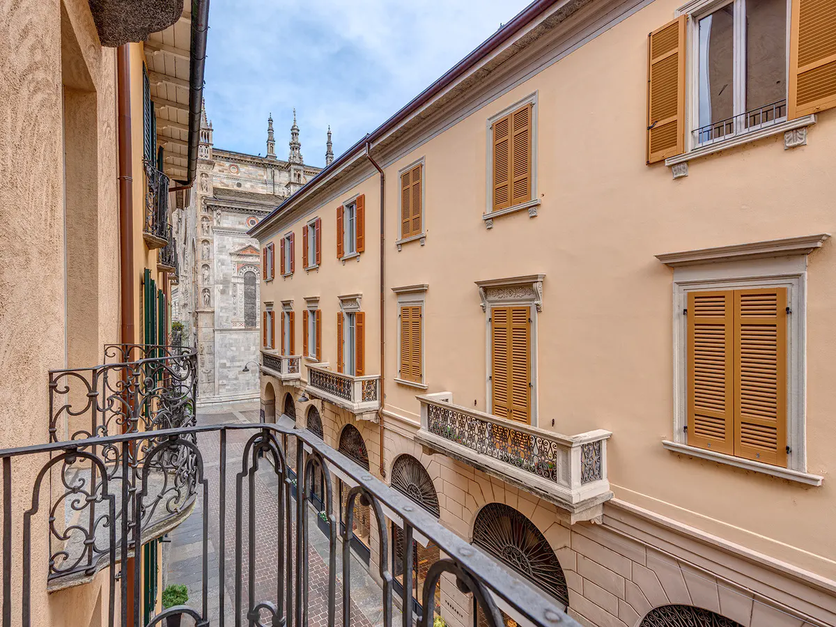 View from a wrought-iron balcony of a peach building with brown shutters, and a church in the background.