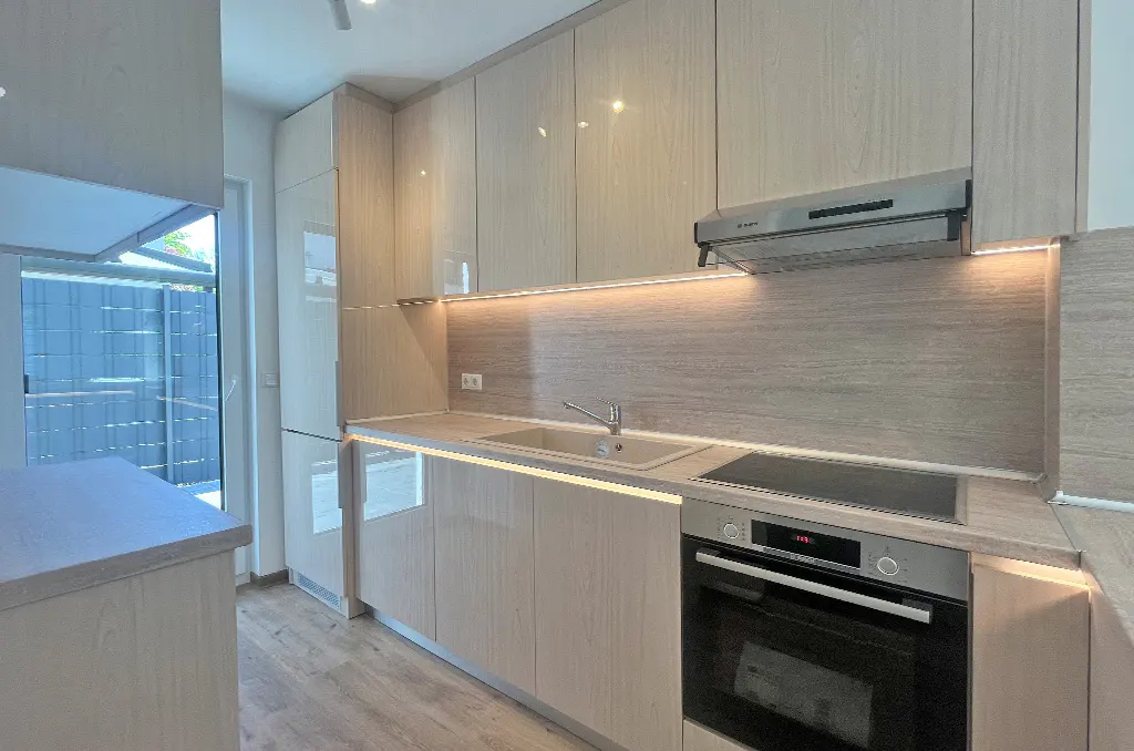 Modern kitchen with light wood cabinets, stainless steel appliances, and under-cabinet lighting. A window provides natural light.
