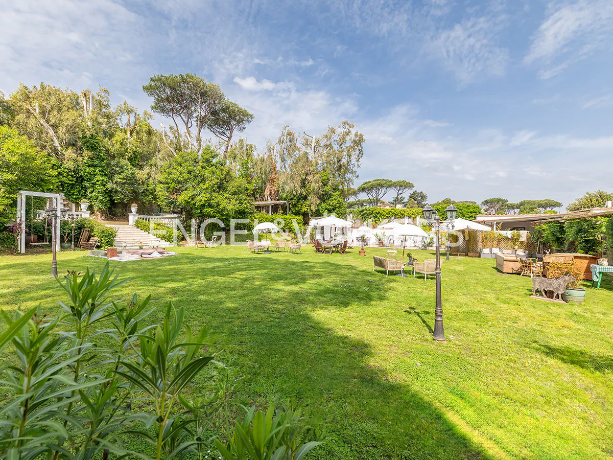 Lush green lawn with trees, white umbrellas, and outdoor seating under a blue sky.