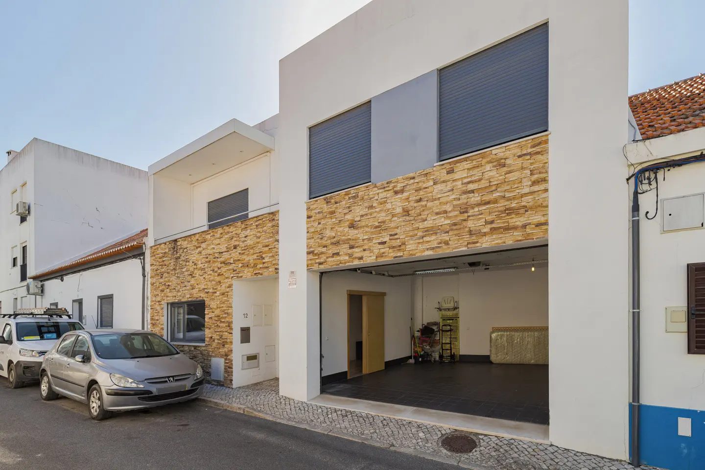 Modern white townhouse with stone facade, open garage, and a silver car parked on a cobblestone street.