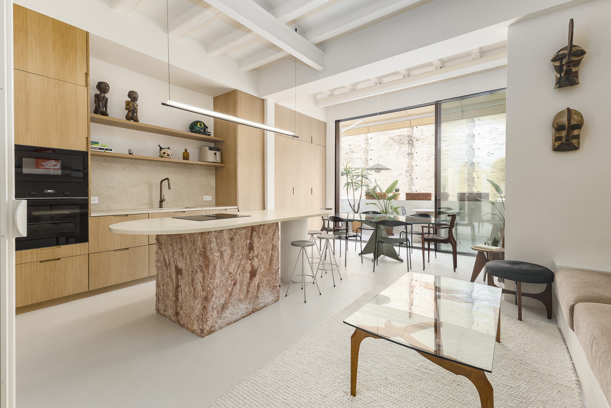 Modern kitchen with light wood cabinets, a textured stone island, glass dining table, and living area with a glass coffee table. [AI-generated text]