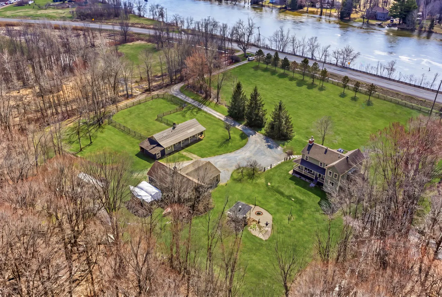 Aerial view of a property with three buildings, green lawns, and a river in the background.