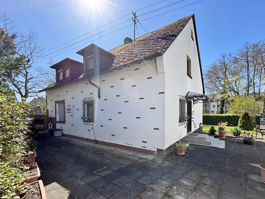 Exterior view of a white house with a brown tiled roof and a stone-paved patio on a sunny day.