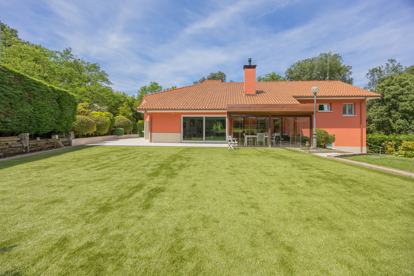 Back view of a peach-colored house with a tiled roof, glass-enclosed patio, and a large, well-manicured green lawn.