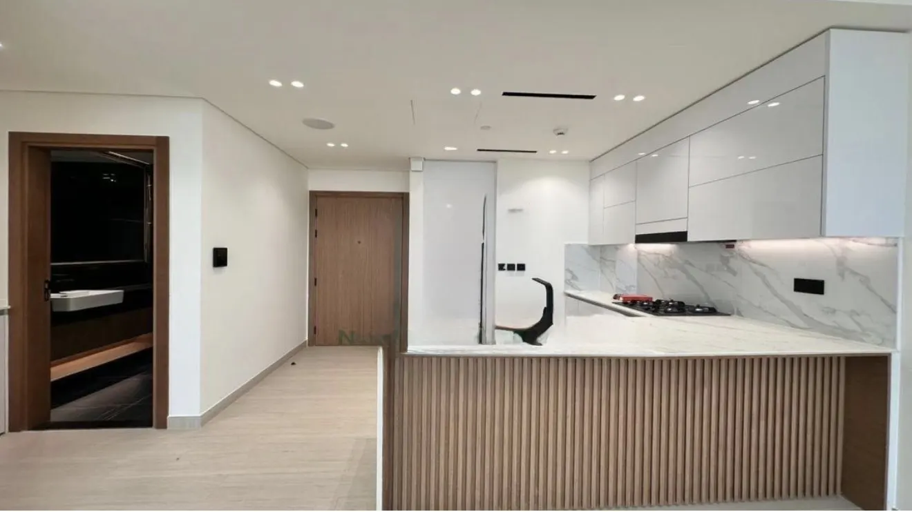 A modern kitchen with white cabinets, marble backsplash, and a wooden-paneled island. A bathroom and hallway are visible in the background.