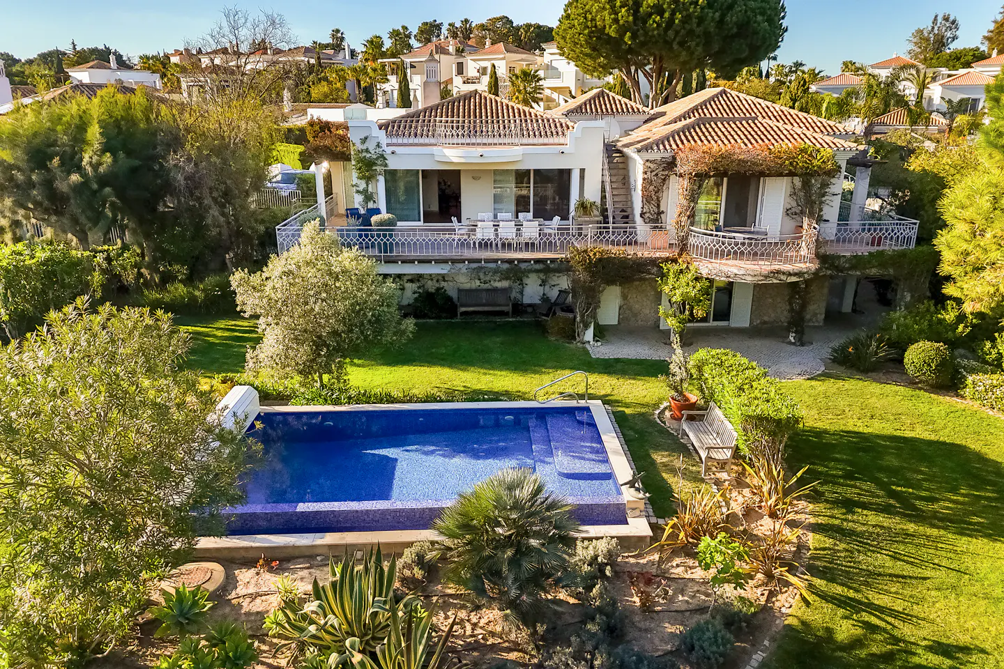 Aerial view of a two-story white house with a red tile roof, a blue swimming pool, and green grass.