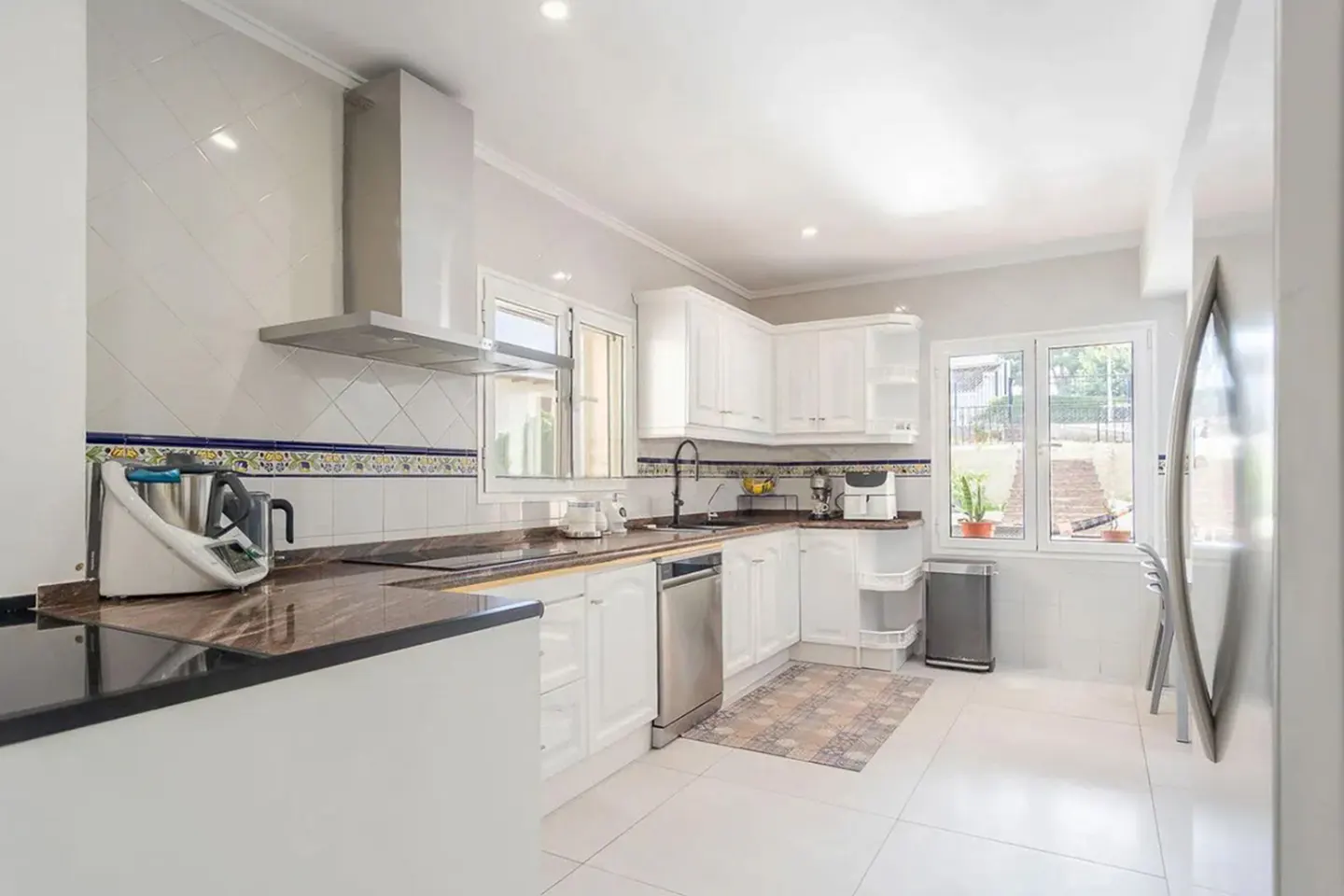 Bright kitchen with white cabinets, stainless steel appliances, and brown marble countertops. A window overlooks a garden.