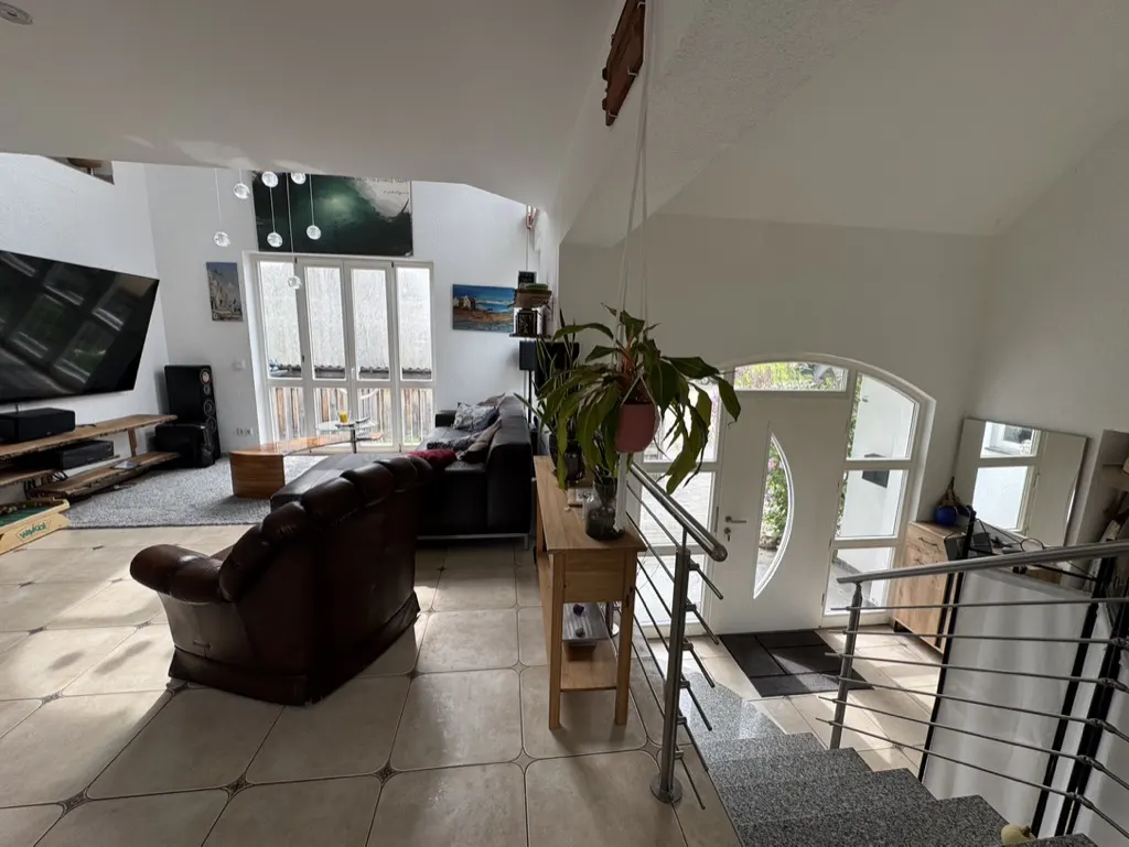 Bright, open living room with a brown leather chair, black sofa, and a staircase leading to a white front door. A hanging plant adds a touch of nature.