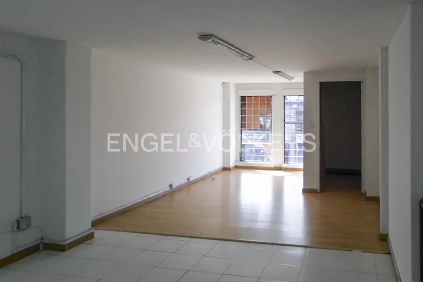 Empty room with white walls, tile and wood floors, and two windows. Engel & Volkers logo on the wall.