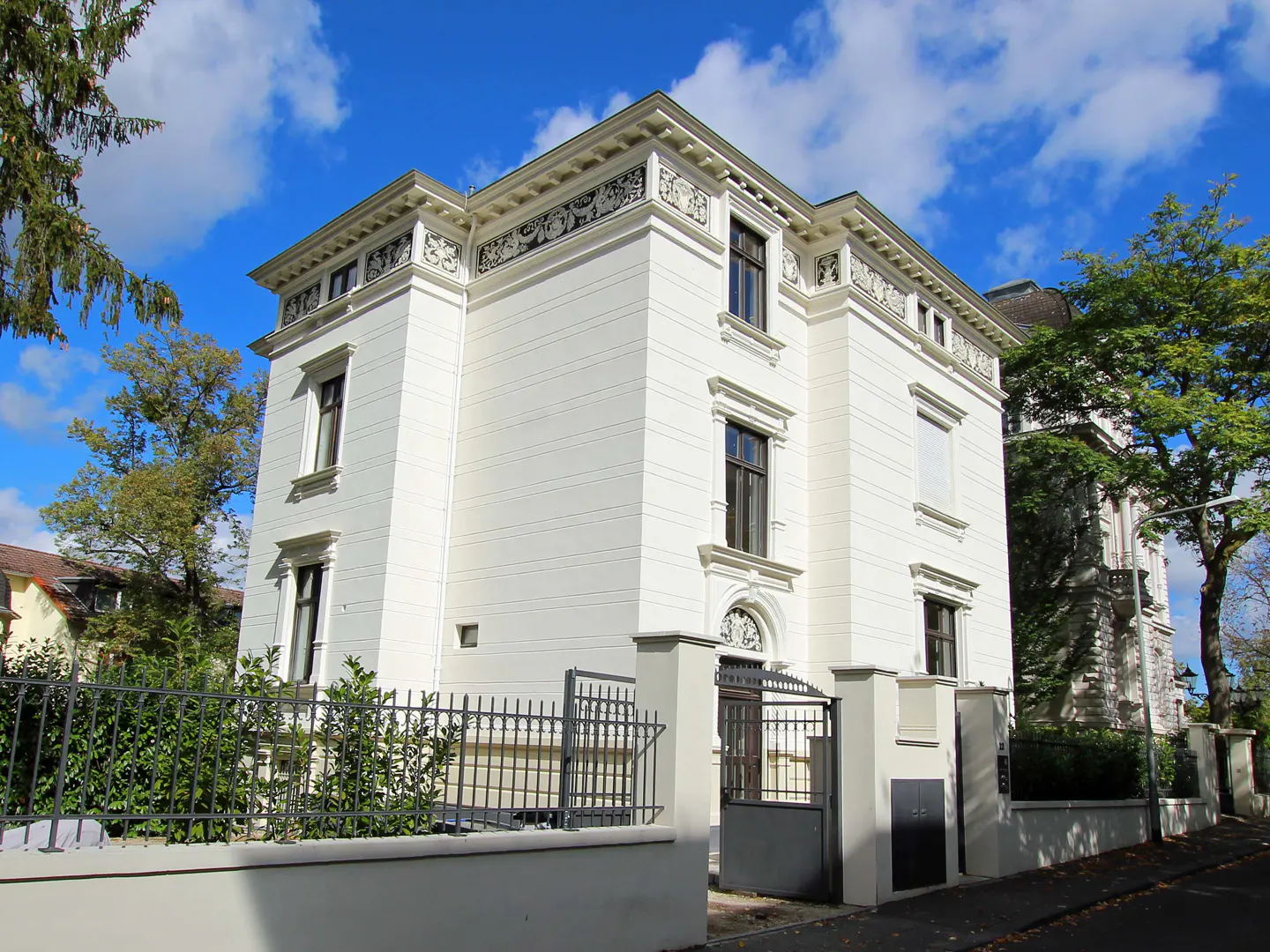 Exterior view of a three-story white house with dark windows, a black iron gate, and a blue sky.