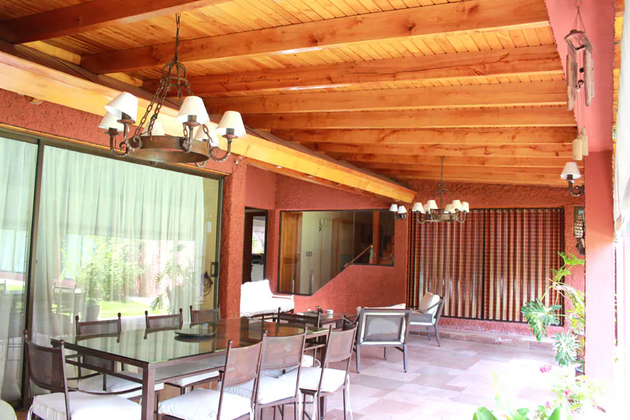 Covered patio with a wood ceiling, a large table with chairs, and a view of the backyard. The walls are textured and painted in a reddish-brown color.
