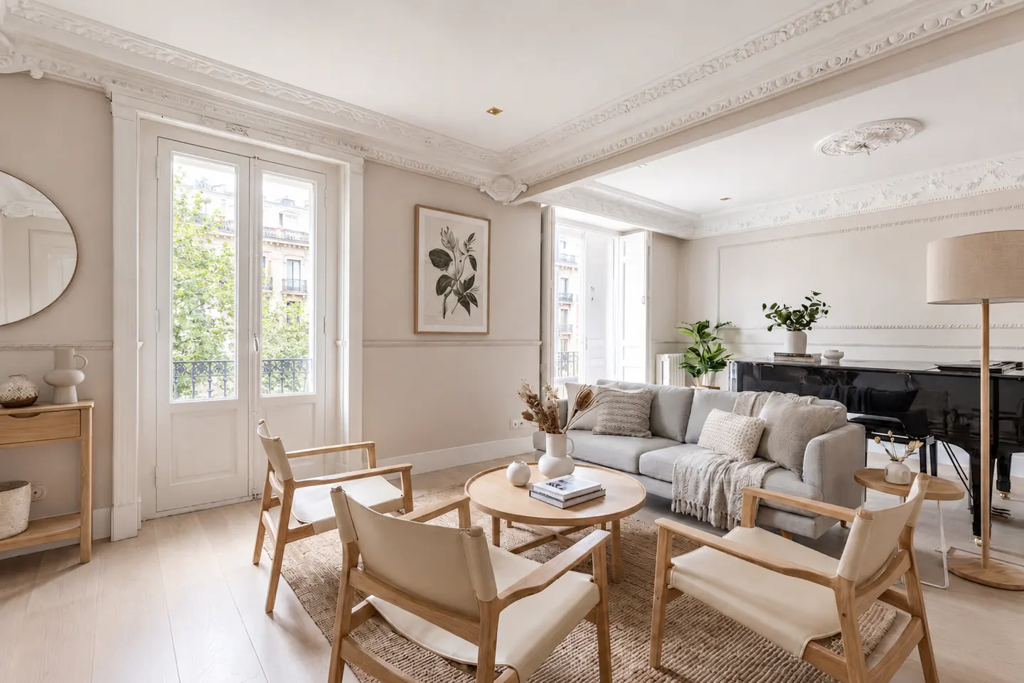 Bright living room with beige walls, white trim, and light wood floors. A gray sofa, wood chairs, and a black piano furnish the space.