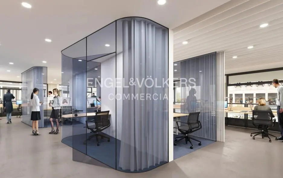 Office space with glass-walled cubicles, desks, and chairs. People are working and talking. Engel & Völkers Commercial logo is visible.