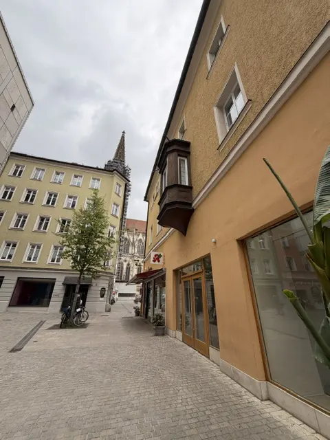 Street view of yellow buildings with white windows and a church steeple in the background on a cloudy day.
