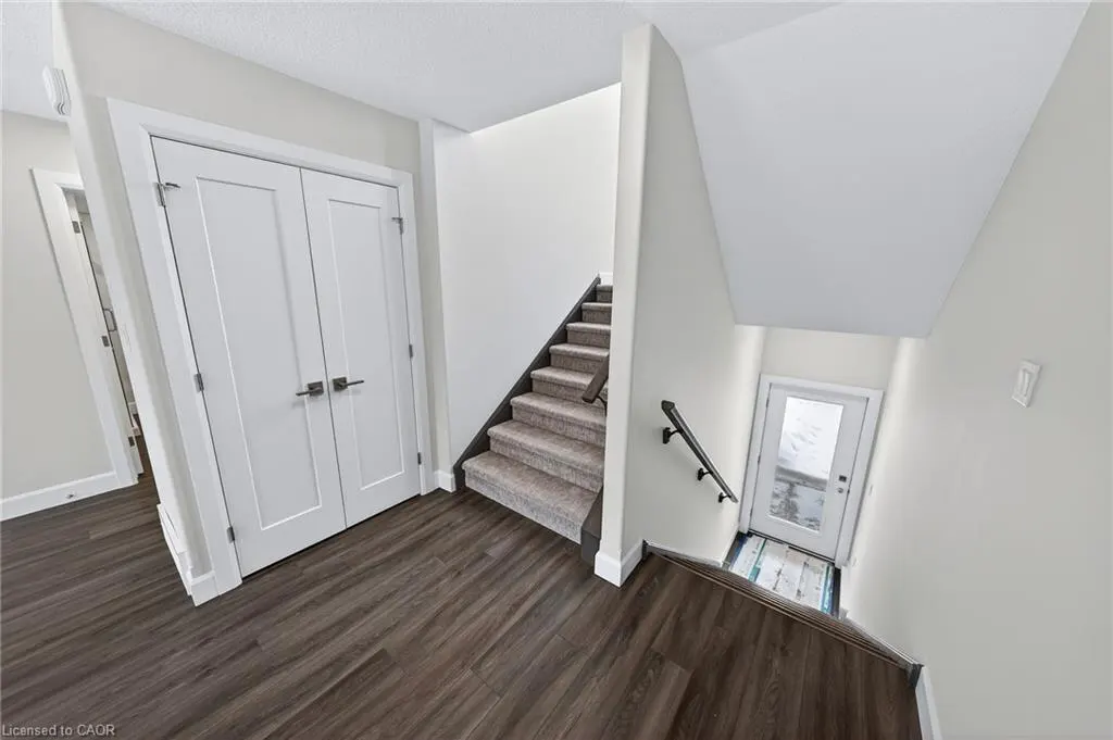 Interior view of a home's entryway with wood floors, white walls, and a carpeted staircase leading to a white door.