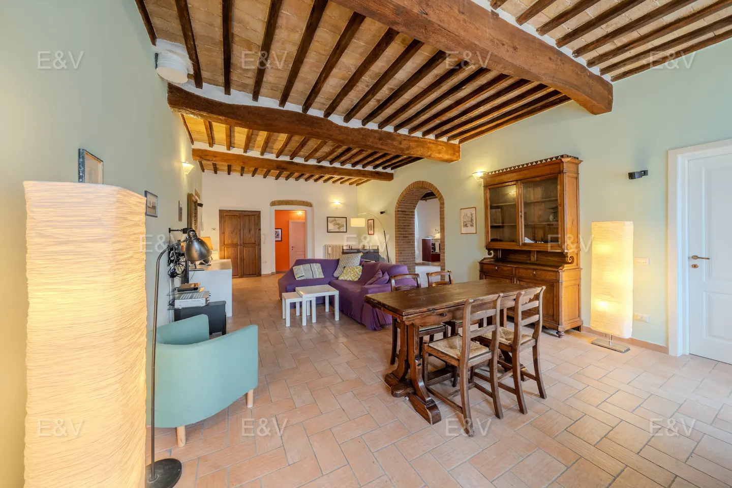 A spacious living room with exposed wood beams, terracotta floors, and a purple sofa.