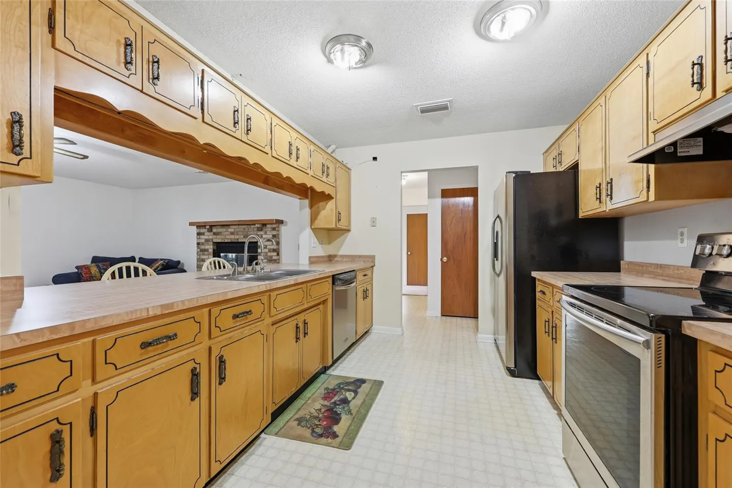 A bright kitchen with light wood cabinets, stainless steel appliances, and a view into the living room.