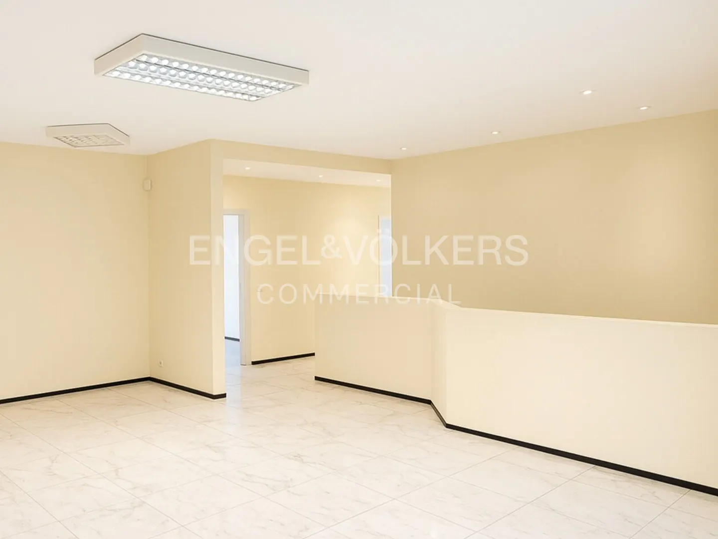 Empty commercial space with beige walls, marble floors, and bright overhead lighting. Doorways lead to other rooms.