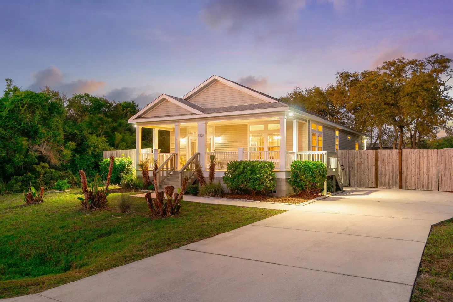 Beige single-story house with a porch, green lawn, and concrete driveway at dusk.