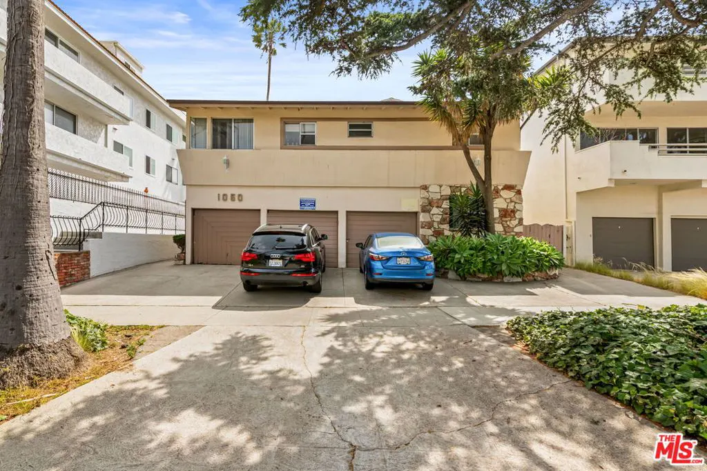 A two-story beige apartment building with three brown garage doors and two parked cars.