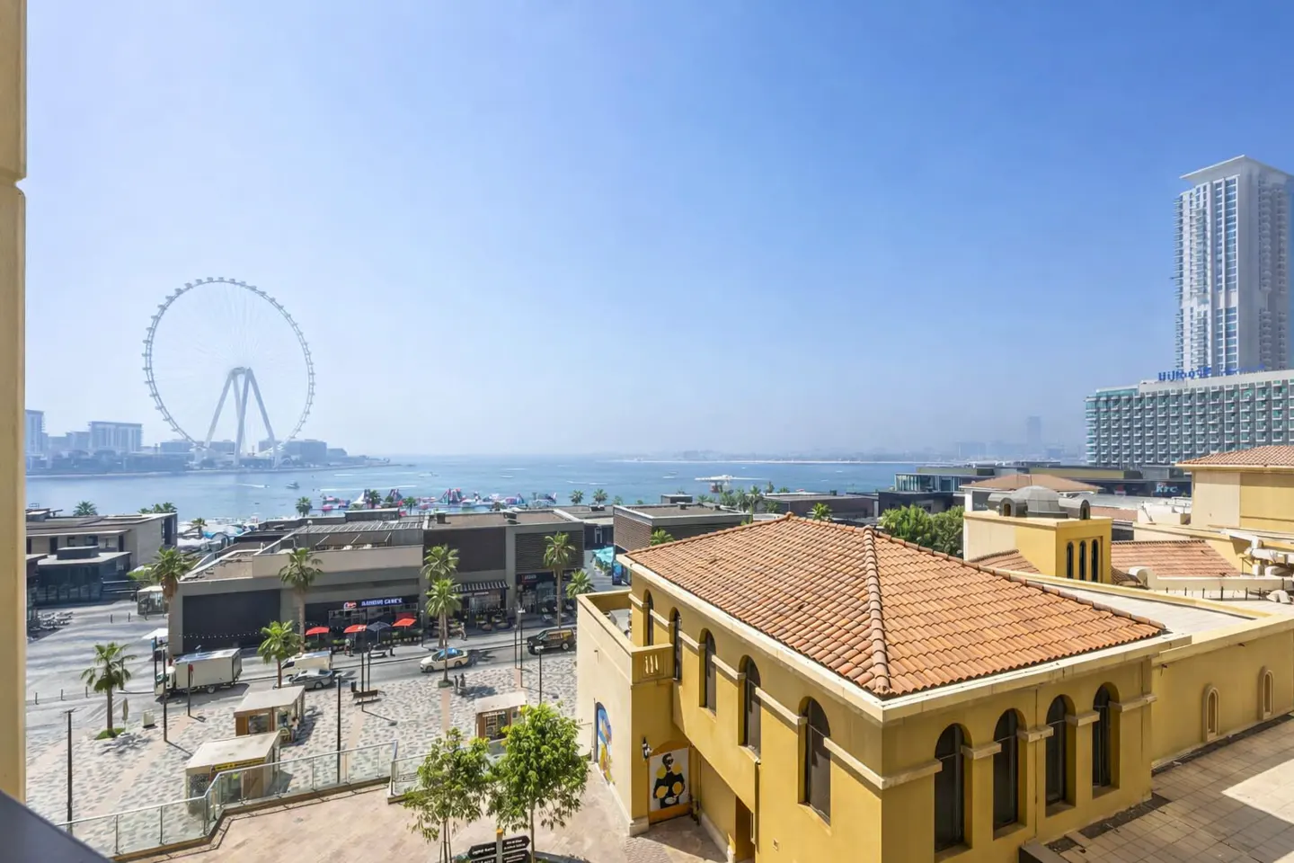 View from a yellow building overlooking a beach with a Ferris wheel and skyscrapers in the distance.