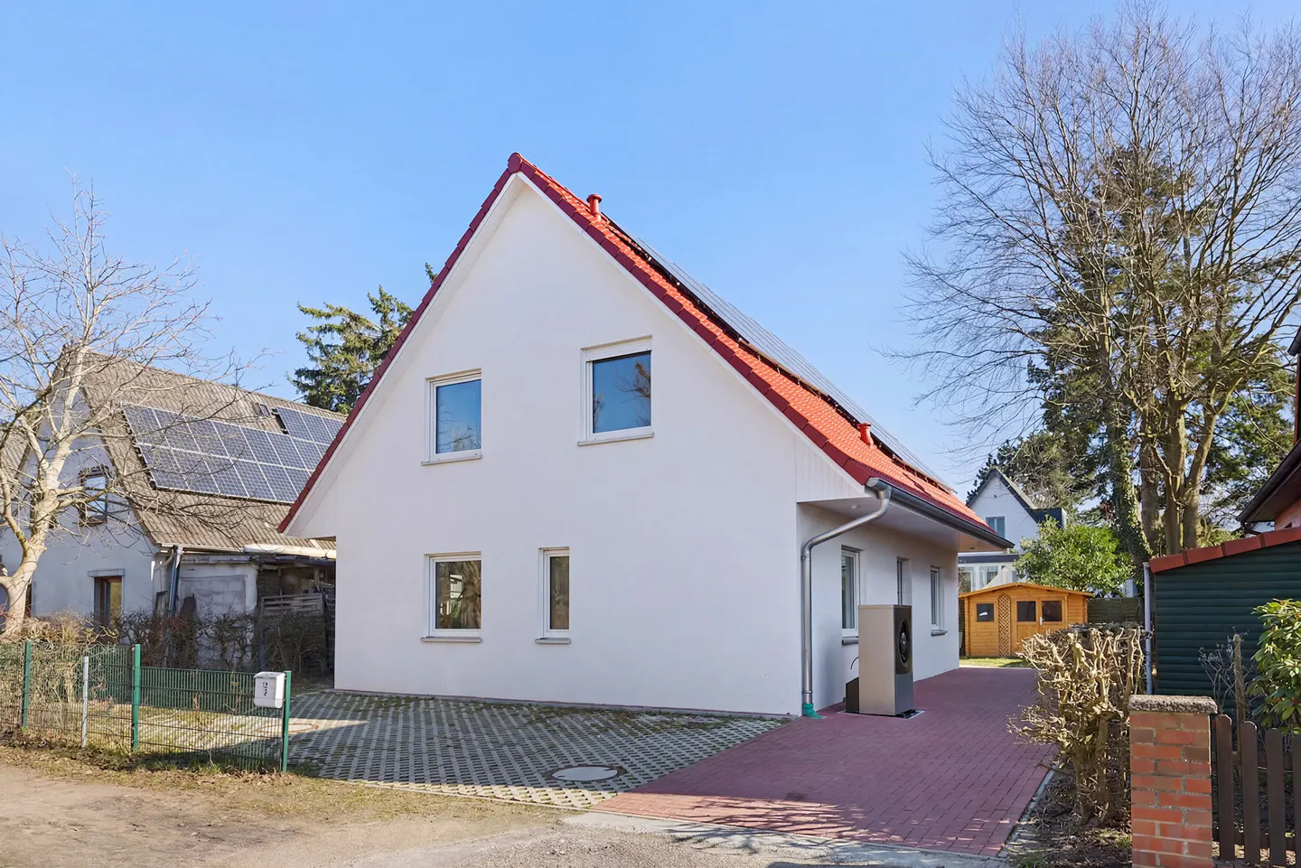 Exterior view of a white, two-story house with a red roof and solar panels. A brick driveway leads to the house.