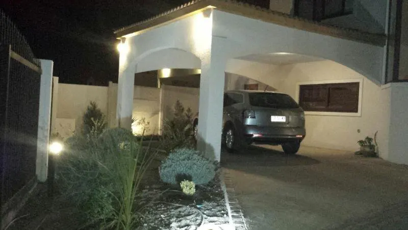 A gray car is parked under a white carport at night. Landscaping is visible in the foreground.