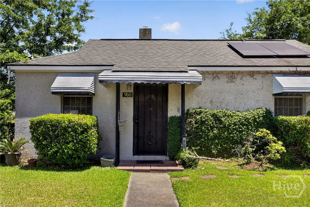 Front view of a one-story house with a gray roof, solar panels, and a dark front door with the number 900 above it.