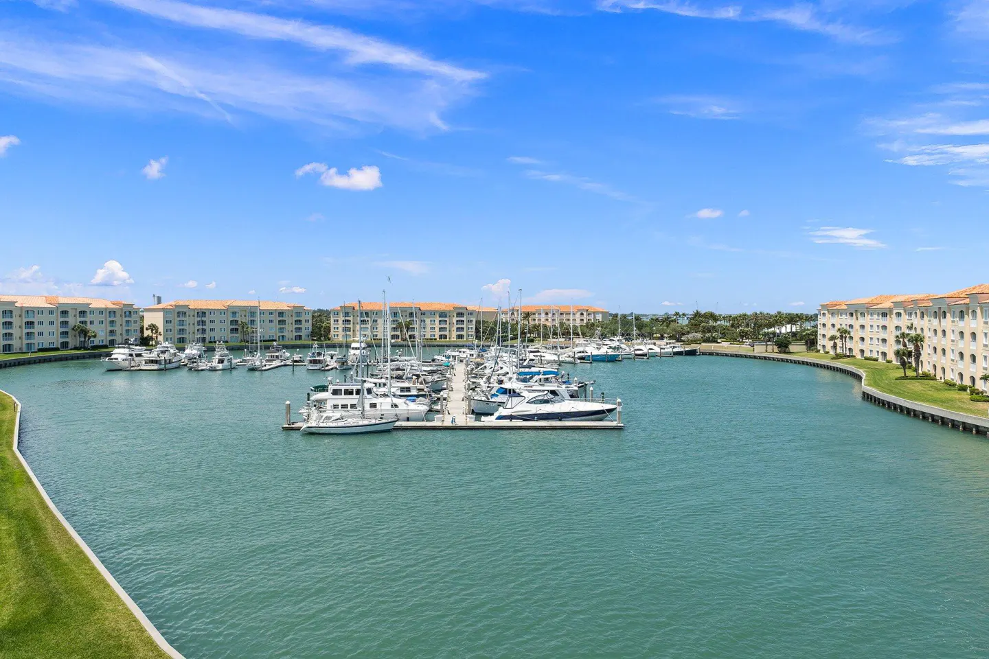 Waterfront condos overlook a marina filled with boats under a blue sky with scattered clouds.