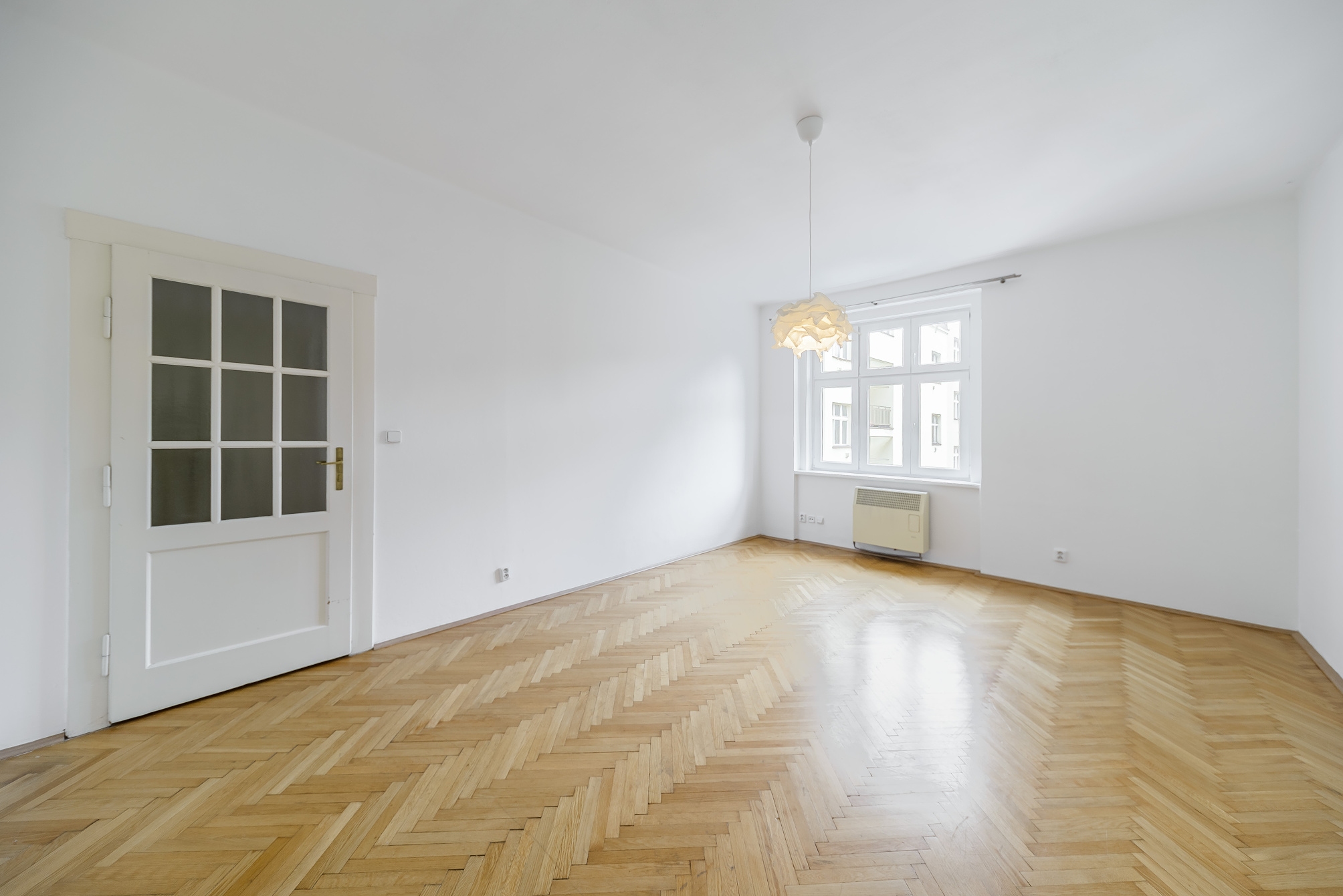 Empty room with white walls, polished herringbone wood floors, a glass-paneled door, and a modern pendant light. [AI-generated text]